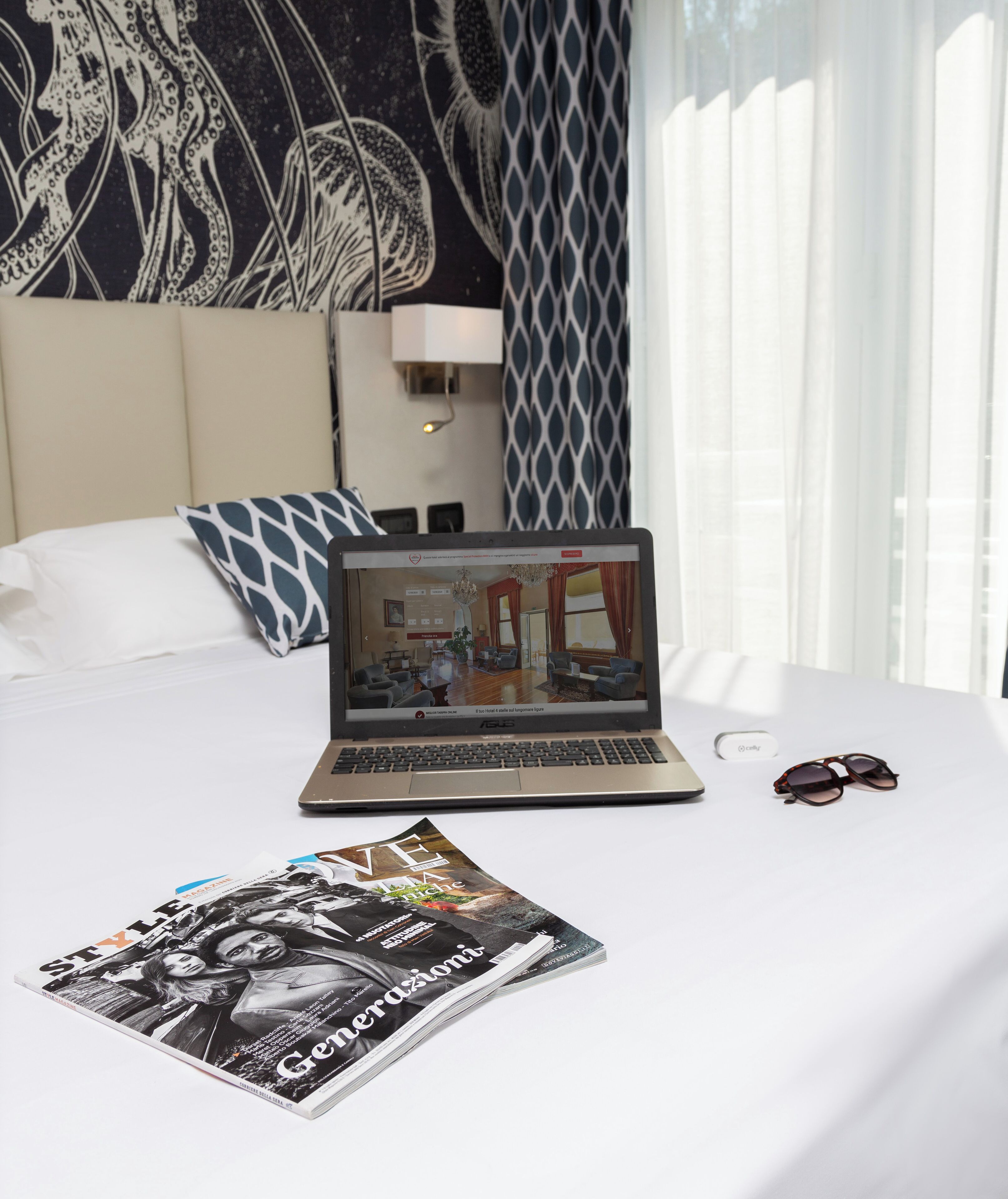 Une chambre d’hôtel avec un lit, un ordinateur portable, un magazine et une paire de lunettes de soleil.