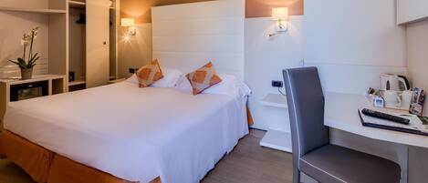 Ein Hotelzimmer mit einem großen Bett, einem Schreibtisch und einem Stuhl. Es gibt einen Kleiderschrank, einen Nachttisch und eine Lampe.