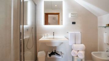 Un baño moderno con ducha de vidrio, un lavamanos blanco con espejo y un bidé.