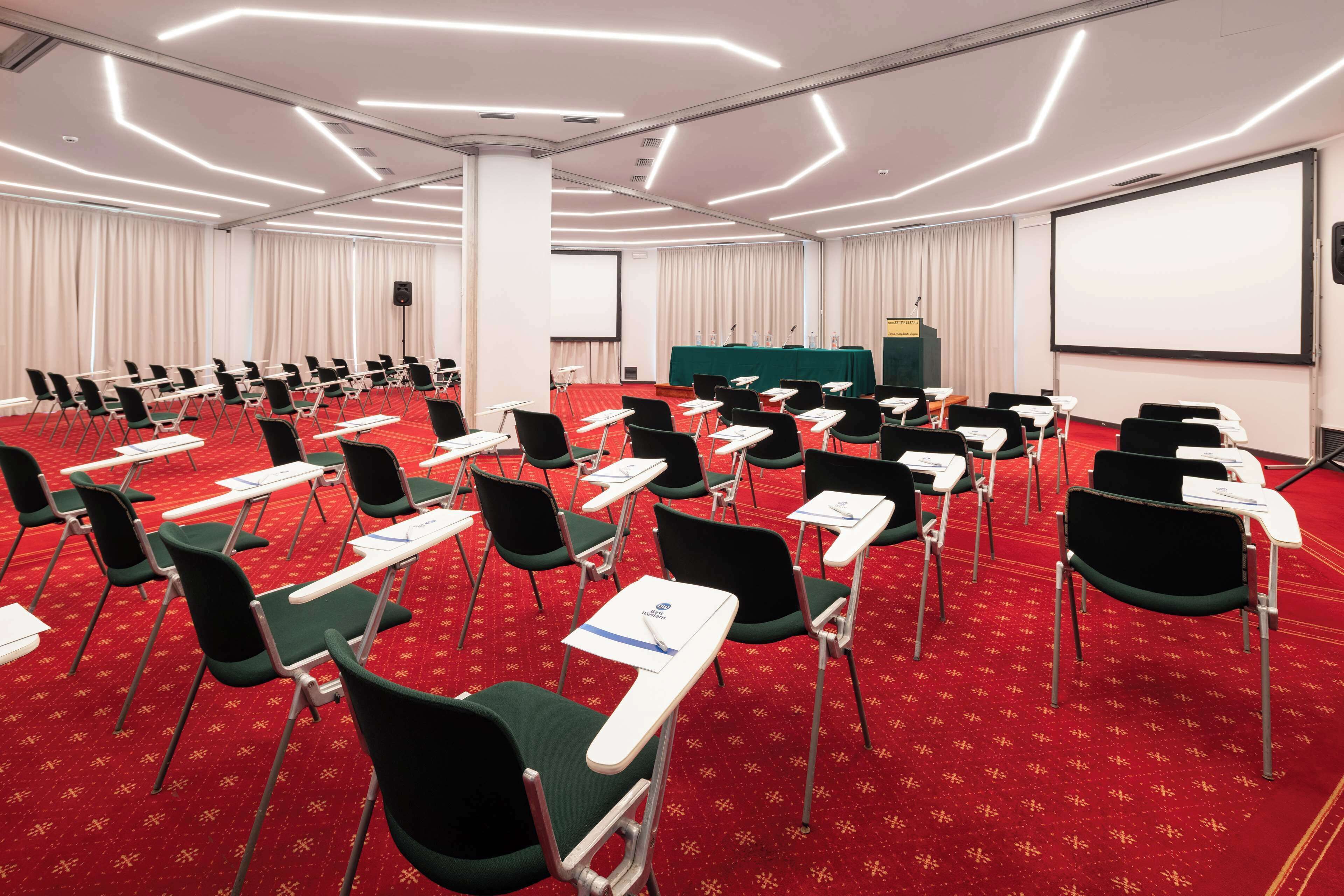A conference room with rows of chairs, a projector screen, and a podium.