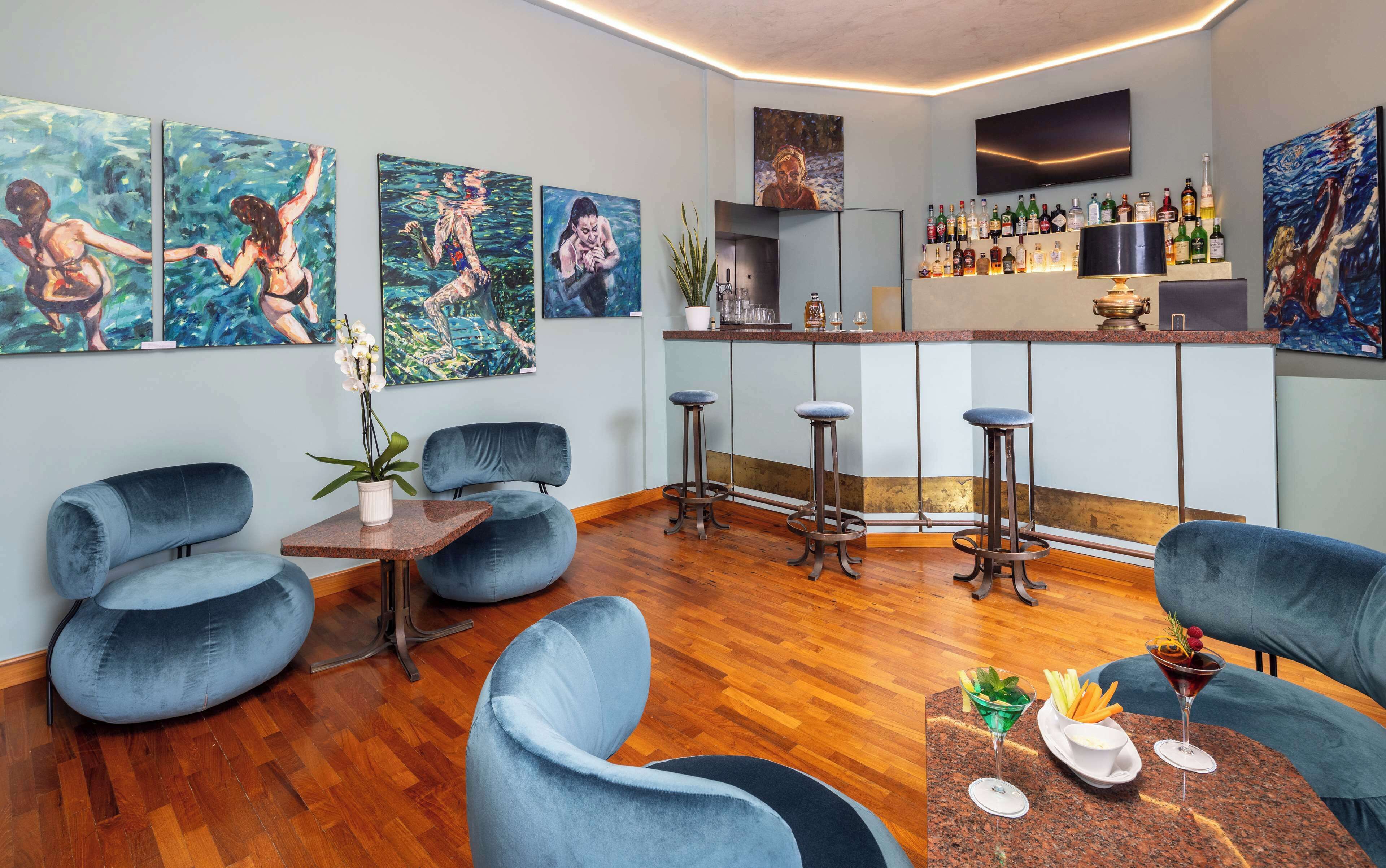 Un área de bar moderna con suelo de madera, sillas tapizadas en azul y una barra con diferentes botellas.