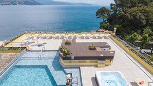 Une piscine sur le toit, avec un jacuzzi, des chaises longues et une vue sur la mer.