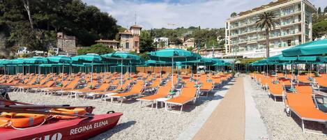 A beachside hotel with rows of sun loungers and umbrellas, a lifeboat, and a building with balconies.