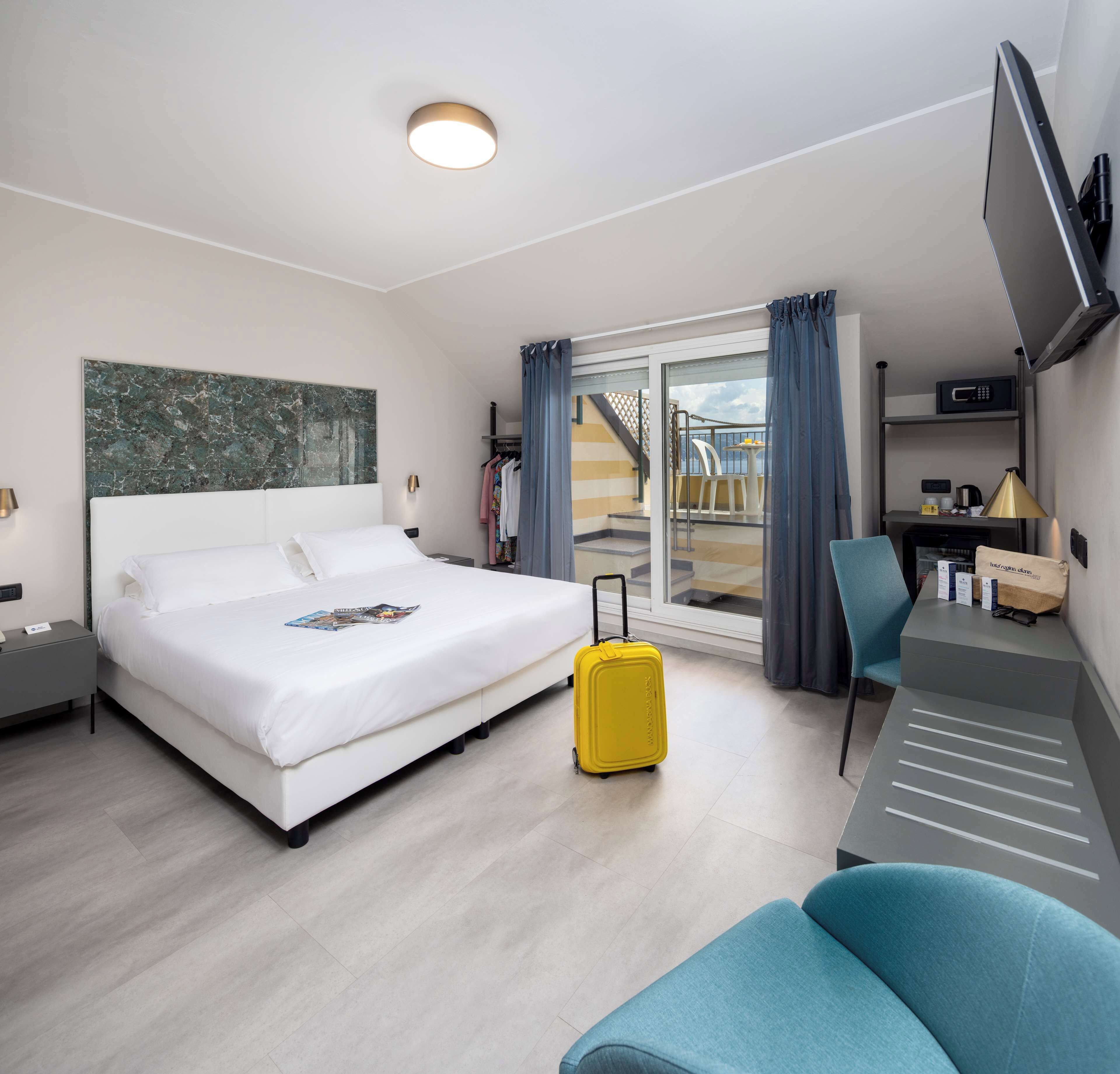 Ein Hotelzimmer mit Bett, Schreibtisch, Stuhl und Koffer, mit Blick ins Freie.