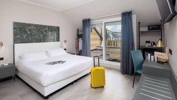 Ein Hotelzimmer mit Bett, Schreibtisch, Stuhl und Koffer, mit Blick ins Freie.