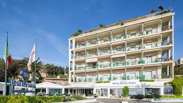 Un hotel de varios pisos con balcones, un cartel de Best Western Hotel Regina Elena y una playa privada con restaurante al aire libre.