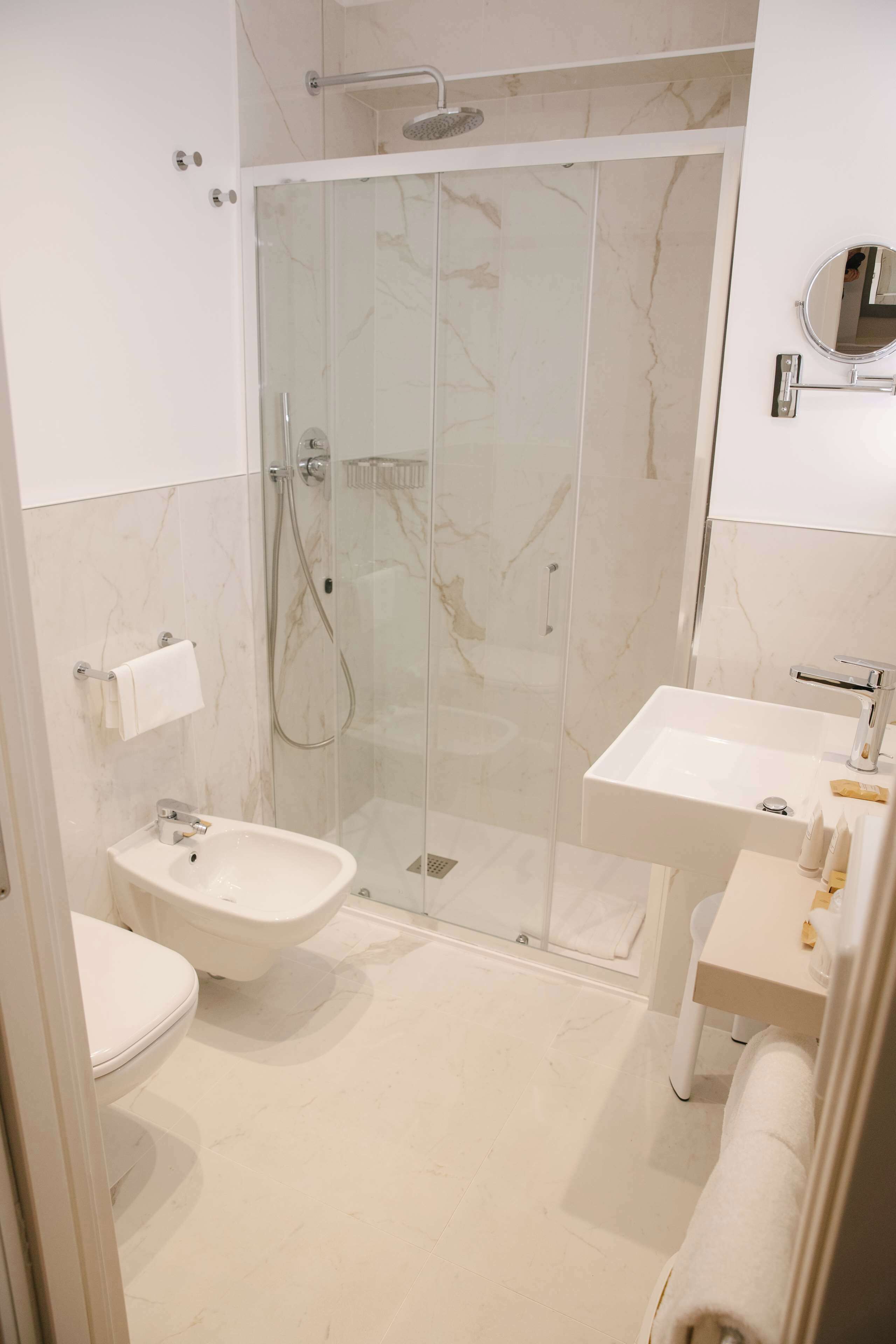 A modern bathroom with a glass-enclosed shower, a pedestal sink, and a toilet.