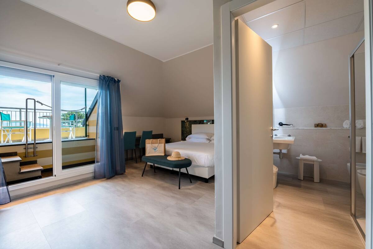 A modern hotel room with a bed, a bathroom, a balcony with a view, and a staircase.
