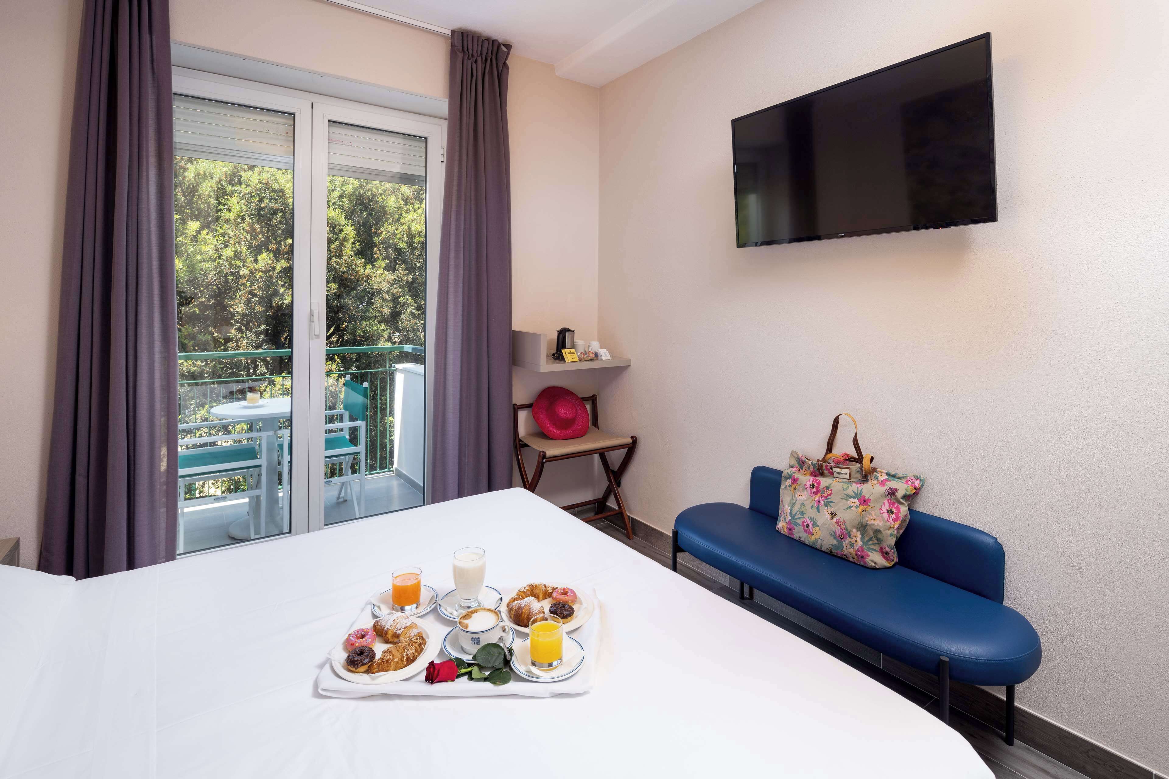 Een hotelkamer met een bed, een ontbijttafel, een televisie, een bank en een balkon met een tafel en stoelen.