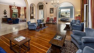A spacious living room with wooden flooring, blue armchairs, a coffee table, and a chandelier.