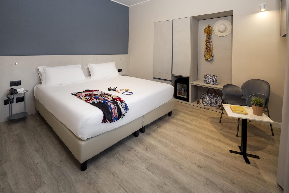 A modern hotel room with a large bed, bedside table, and a small desk with a chair.