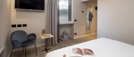A hotel room with a bed, a TV mounted on the wall, a chair, a small table with a plant, and a view of the outside through a window.