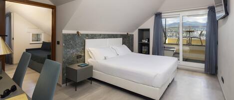 A bedroom with a large bed, a desk with a chair, a nightstand, and a view of the city through a balcony.