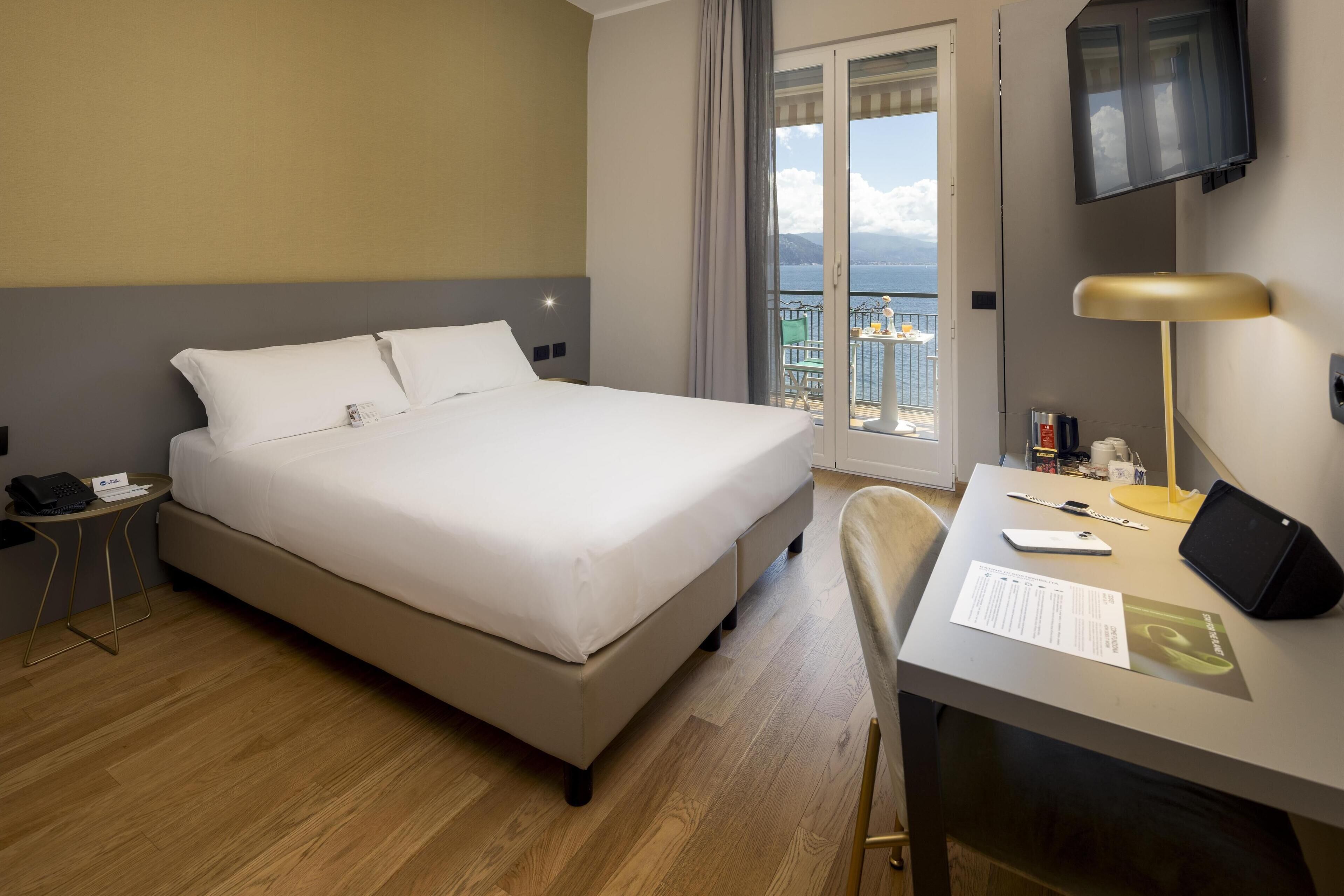 A hotel room with a bed, desk, chair, and a view of the sea.