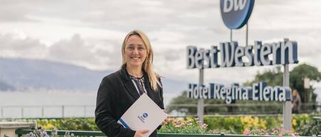 A person holding a booklet in front of a sign for BestWestern Hotel Regina Elena.