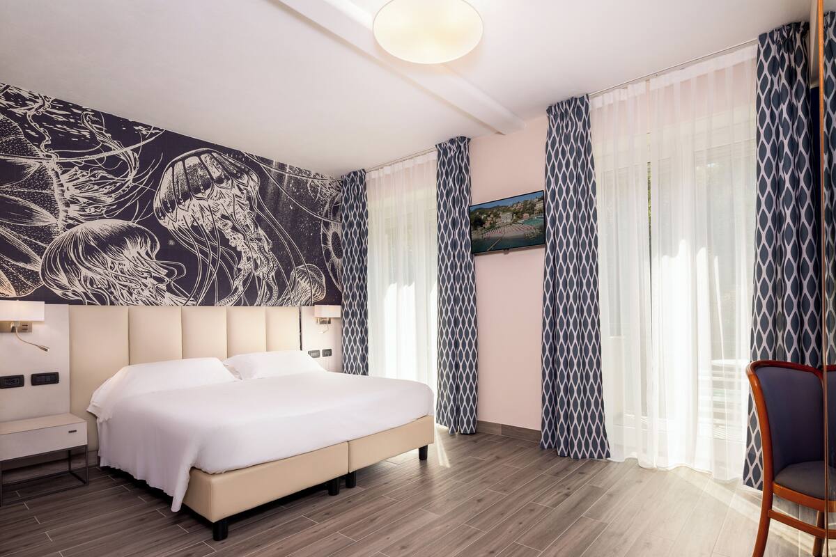 A modern hotel room with a large bed, a wall mural, and patterned curtains.