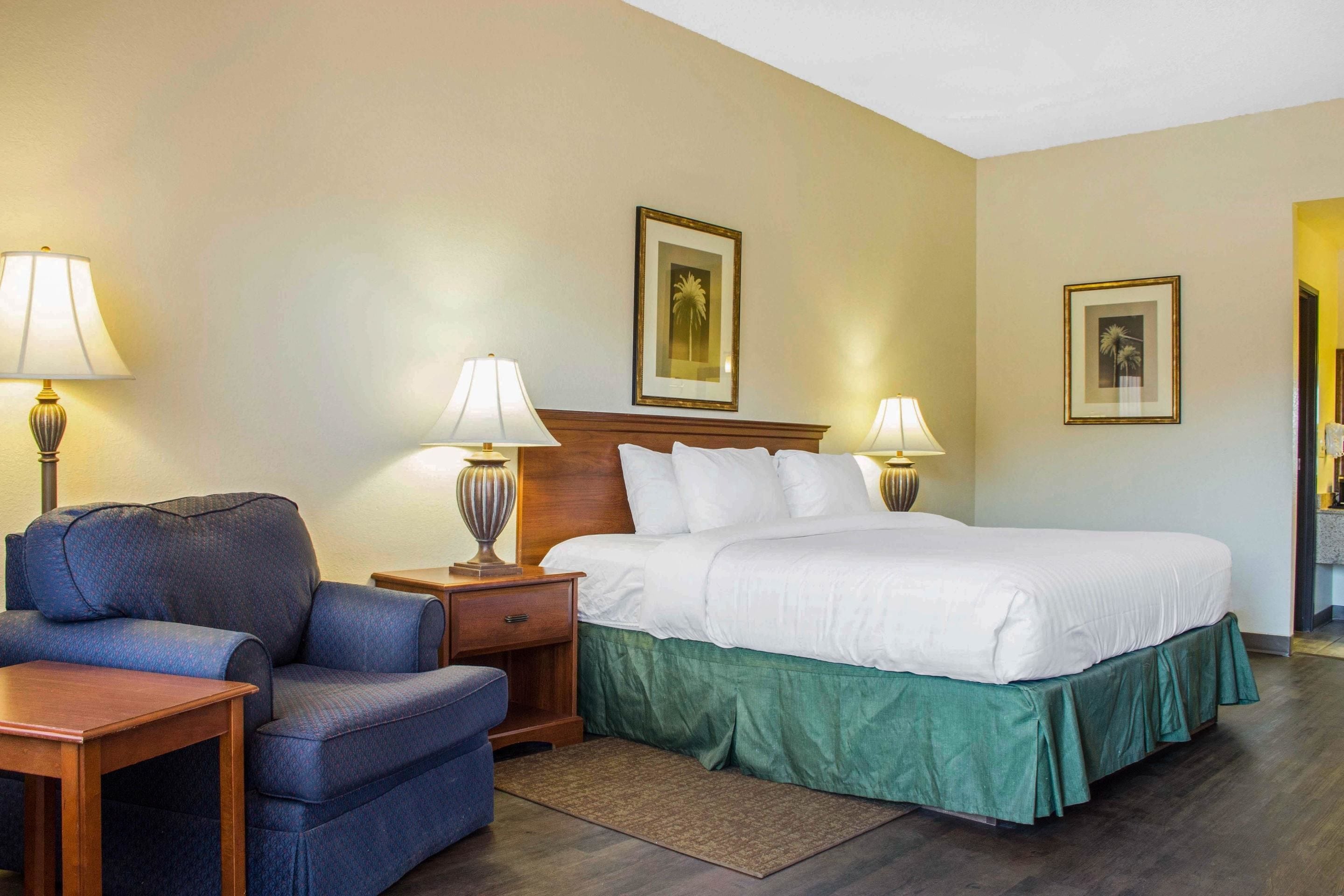 A hotel room with a bed, a chair, a nightstand, and two lamps.