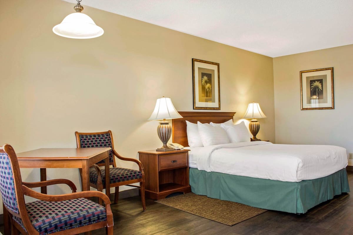 A hotel room with a bed, two bedside tables with lamps, a wooden desk with a chair, and two framed pictures on the wall.
