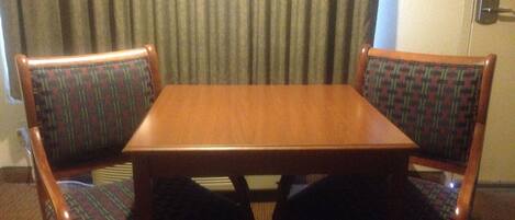 A wooden table with two upholstered chairs in a room with a curtain backdrop.