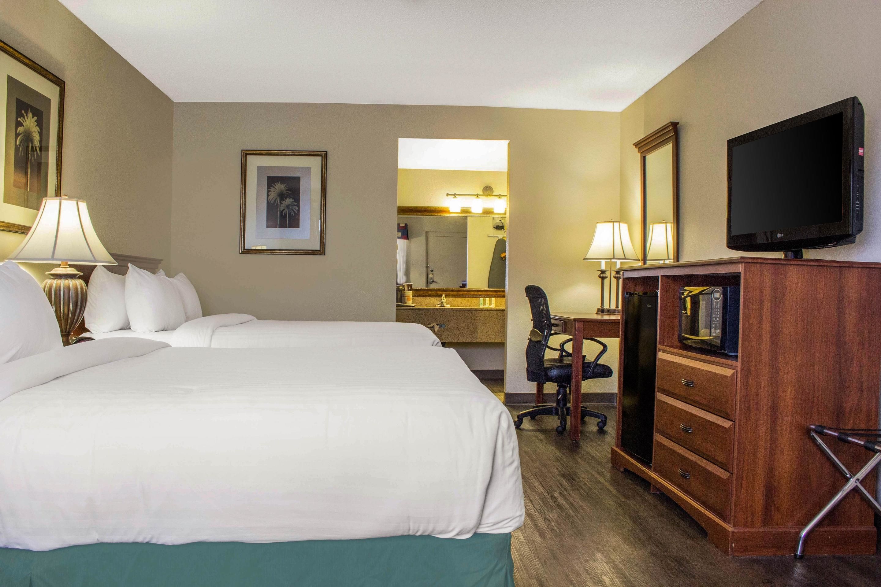 A hotel room with a large bed, a desk with a chair, a television, and a mirror.