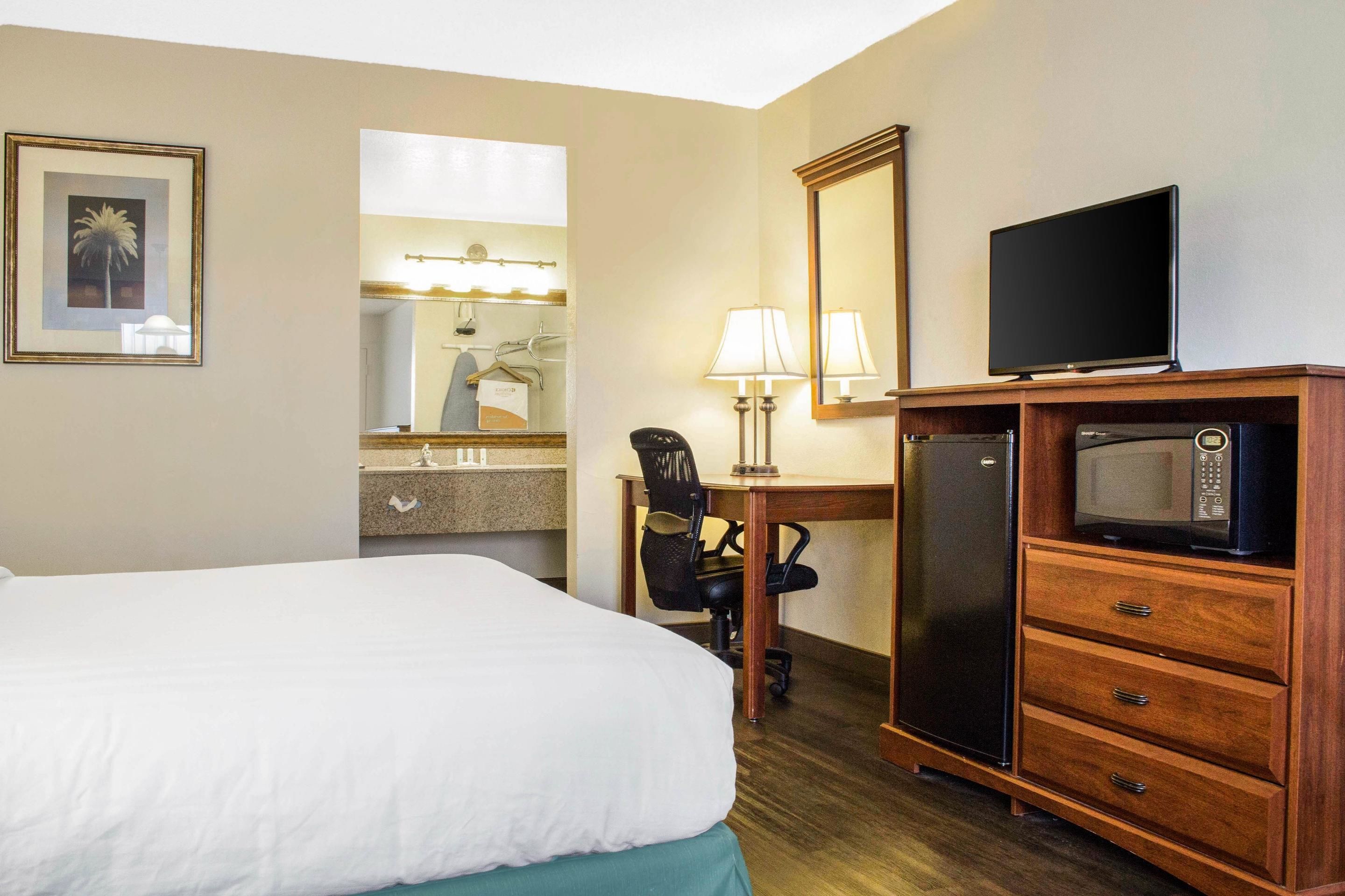 A hotel room with a bed, a desk with a computer, a television, a microwave, and a mirror.