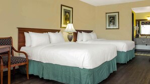 Una camera d'albergo con due letti, una scrivania, una sedia e un comodino con una lampada.