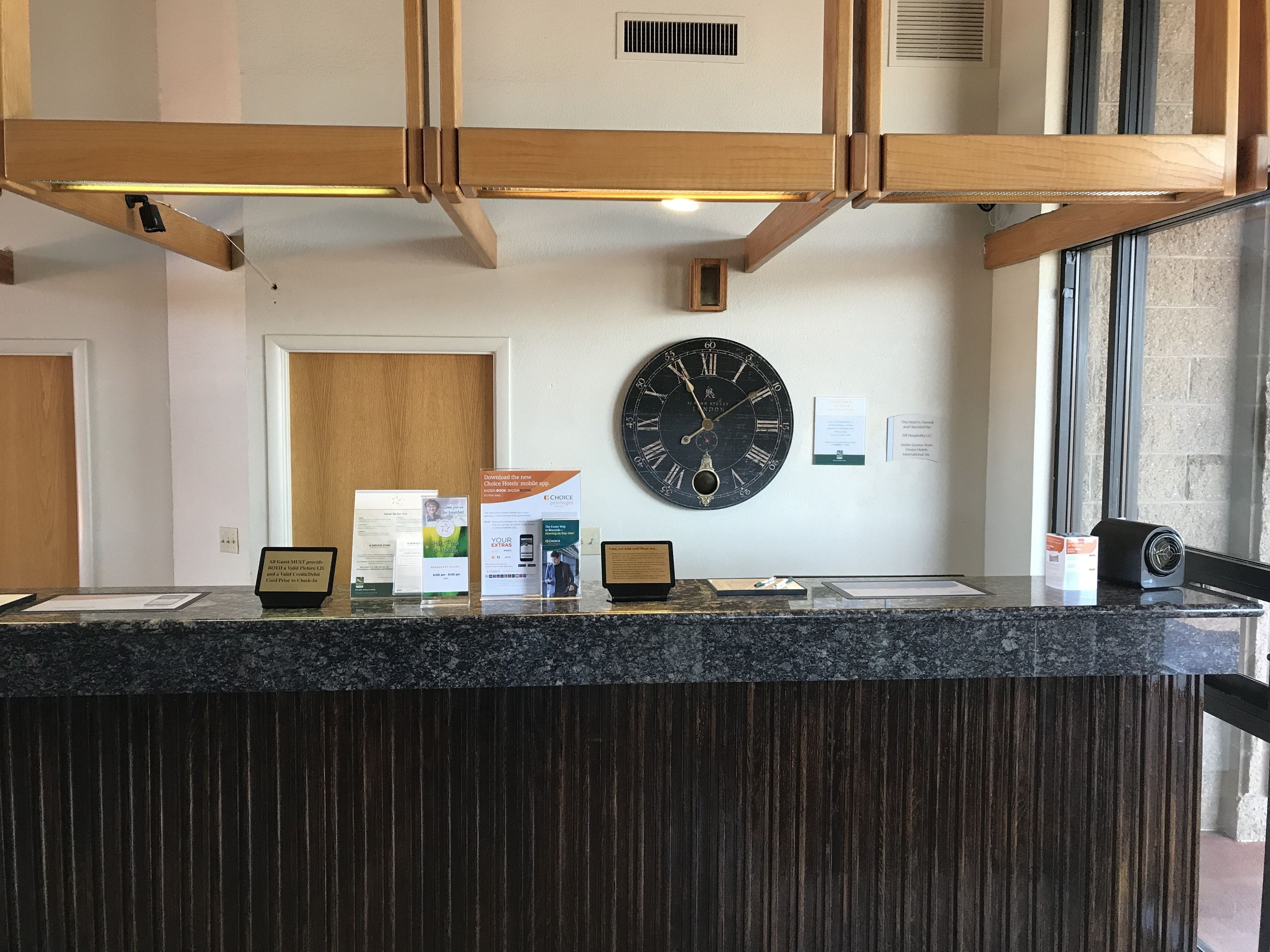 A reception desk with a clock, informational posters, and a window with blinds.