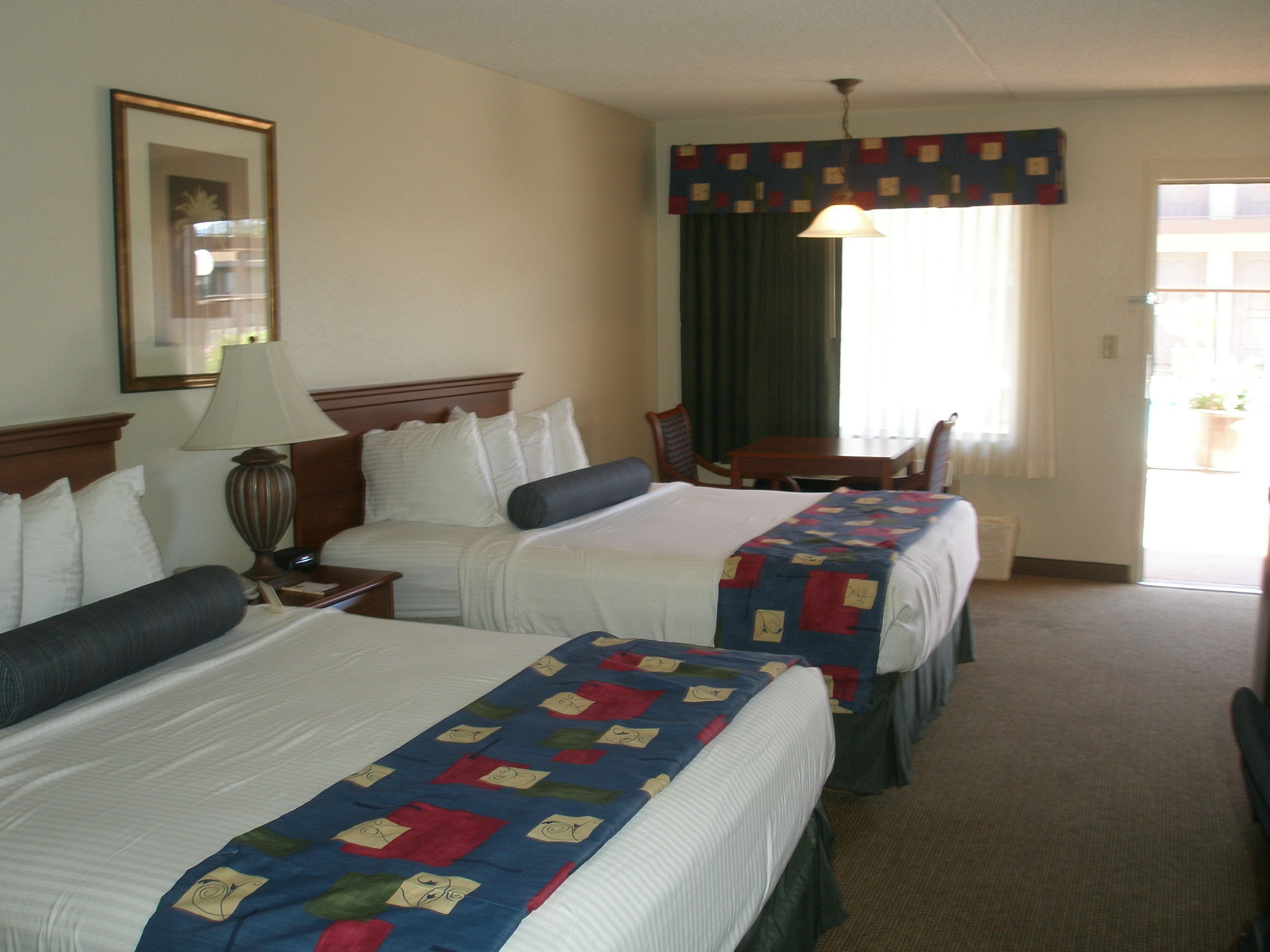 A hotel room with two beds, a desk, a chair, a lamp, and a window with curtains.