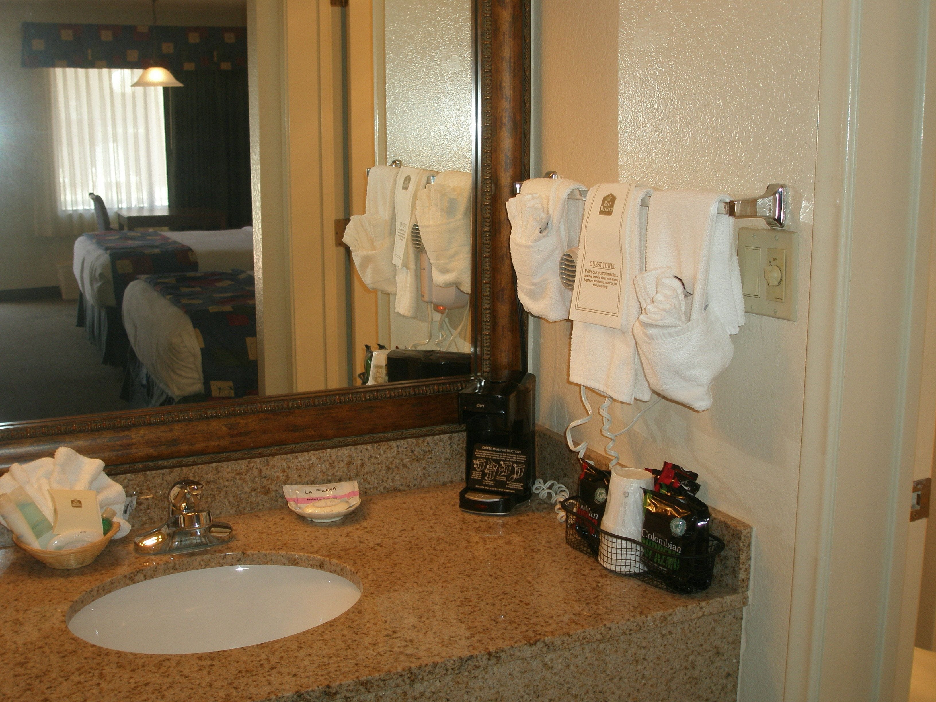 A hotel bathroom with a granite countertop, a sink, a mirror, and a towel rack with multiple towels.