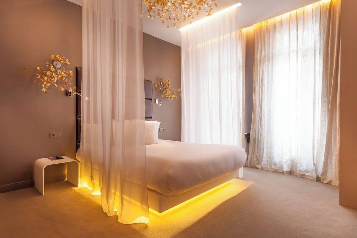 Een moderne slaapkamer met een groot bed, dunne gordijnen en sfeervolle verlichting.