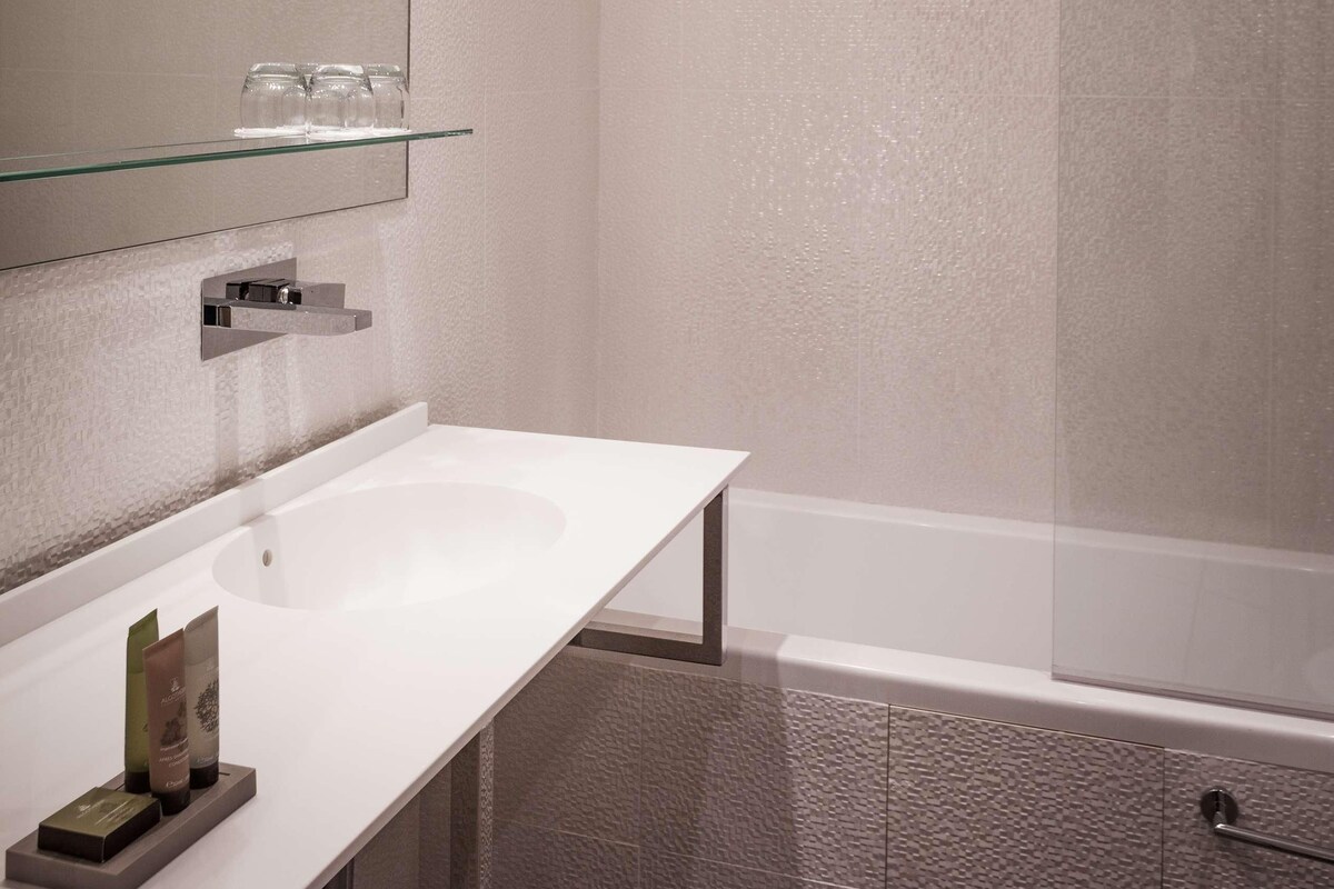 Ein modernes Badezimmer mit einem weißen Waschbecken, einer Glasablage für Toilettenartikel, einem großen Spiegel und einer Duschkabine.