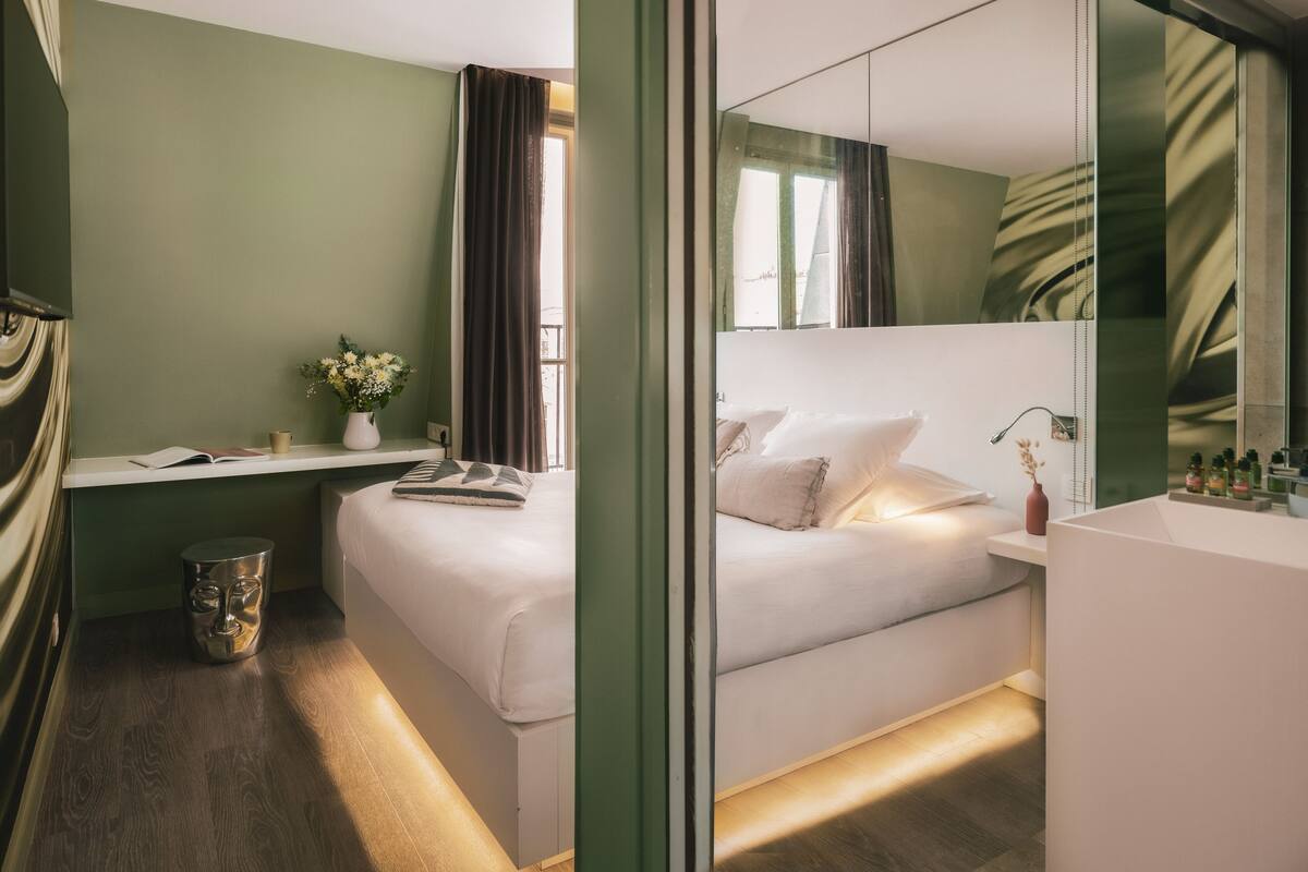 Een moderne hotelkamer met een bed, nachtkastje en een grote spiegel.