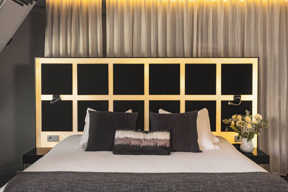 Een moderne hotelkamer met een groot bed, een hoofdbord met een rasterpatroon en een nachtkastje met een bloevas.