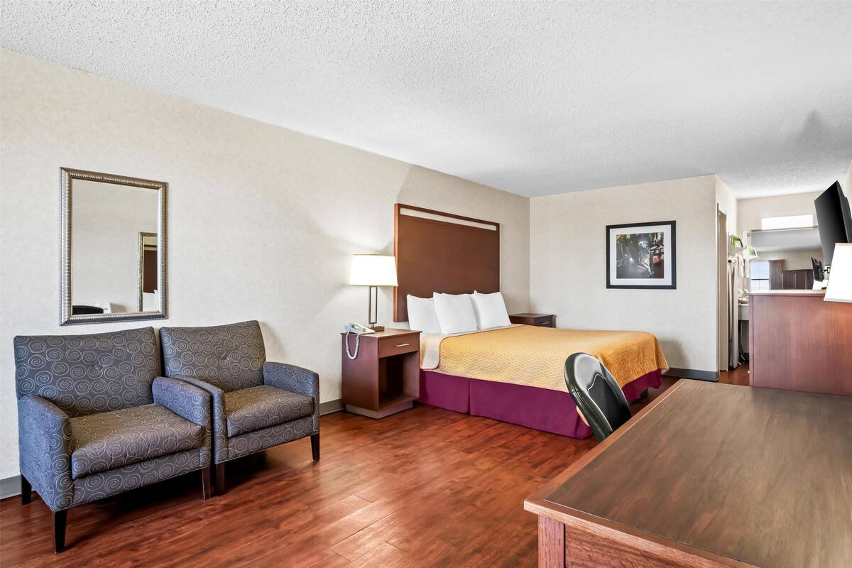 A hotel room with a bed, a sofa, a desk, and a mirror.