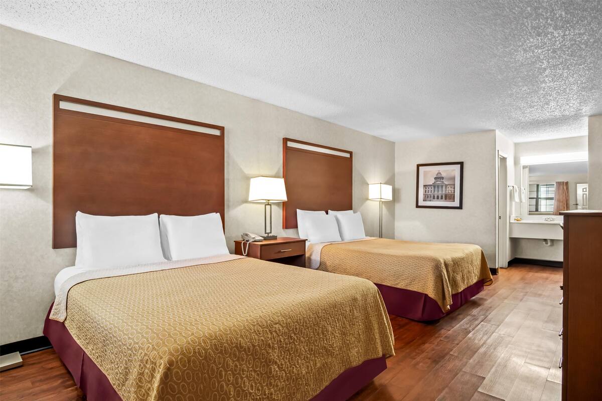 A hotel room with two beds, a desk, a chair, a lamp, and a framed picture on the wall.