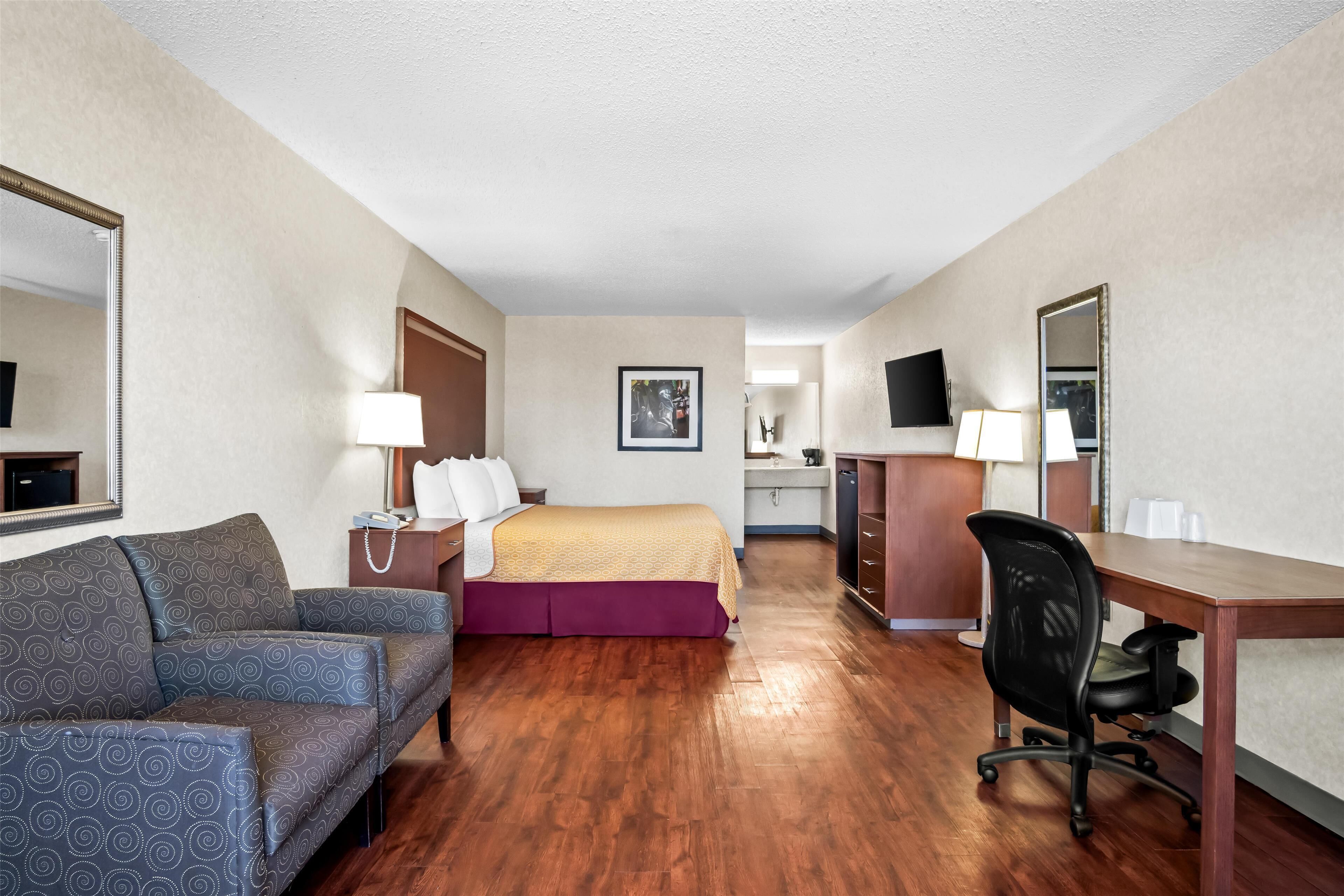 A hotel room with a sofa, a bed, a desk, a chair, a TV, and a bathroom visible in the background.