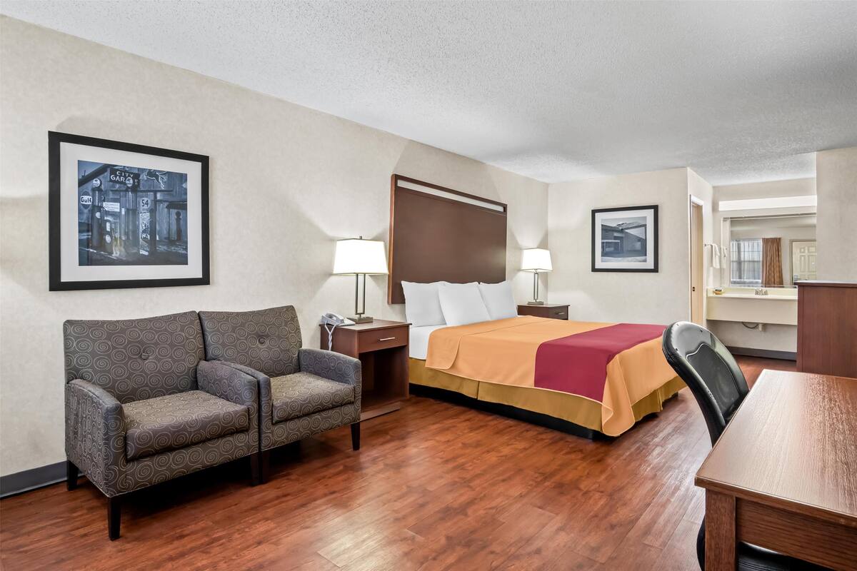 A hotel room with a bed, a sofa, a desk, and a chair. There are two lamps on the nightstands.