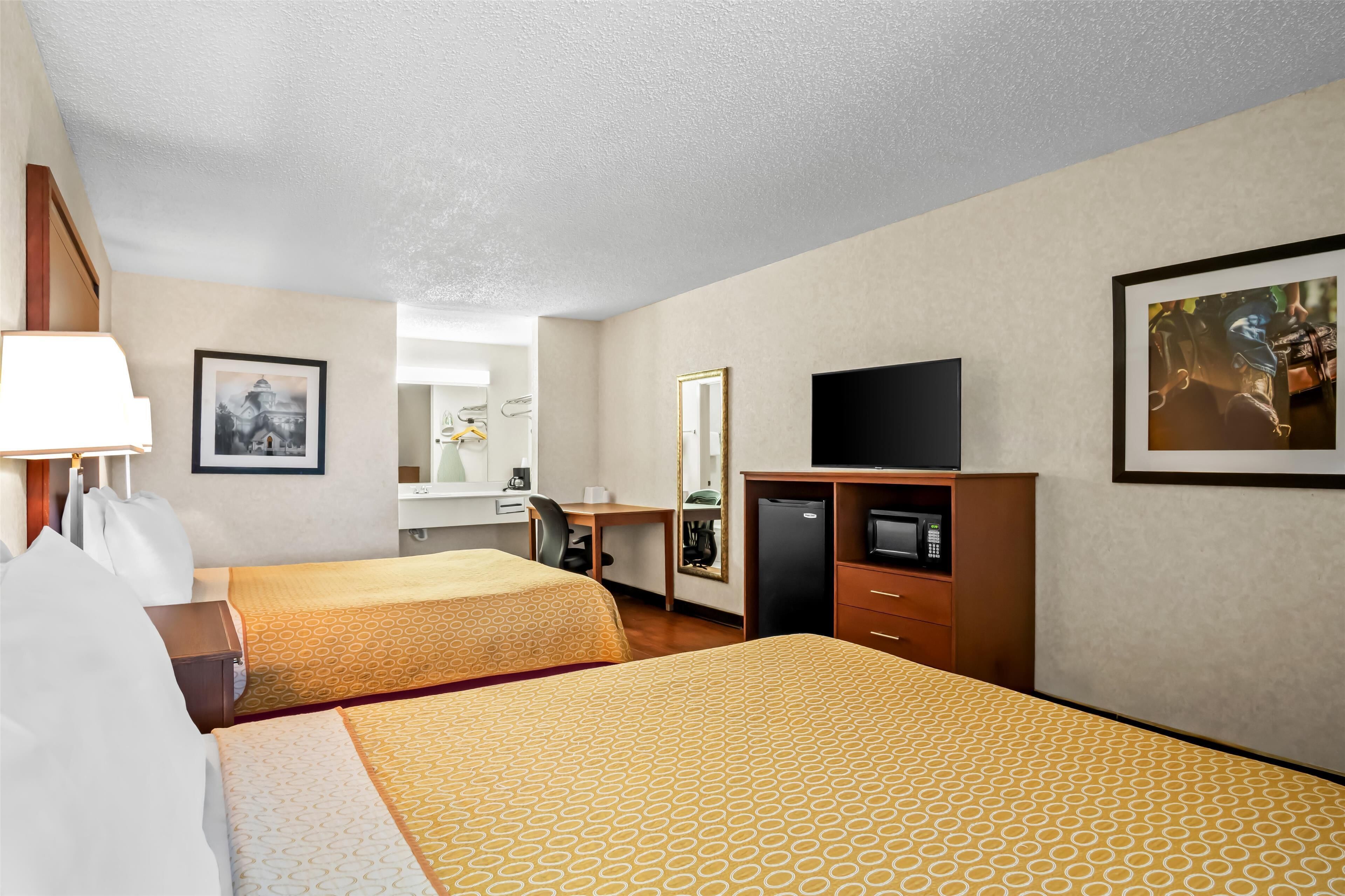 Habitación de hotel con dos camas, un escritorio, un televisor y un espejo.