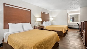 Une chambre d’hôtel avec deux lits, des têtes de lit en bois, des lampes de chevet, un bureau et un miroir.