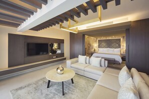 Una sala moderna con sofá, una mesa de centro, televisor y un dormitorio con cama y mesita de noche.