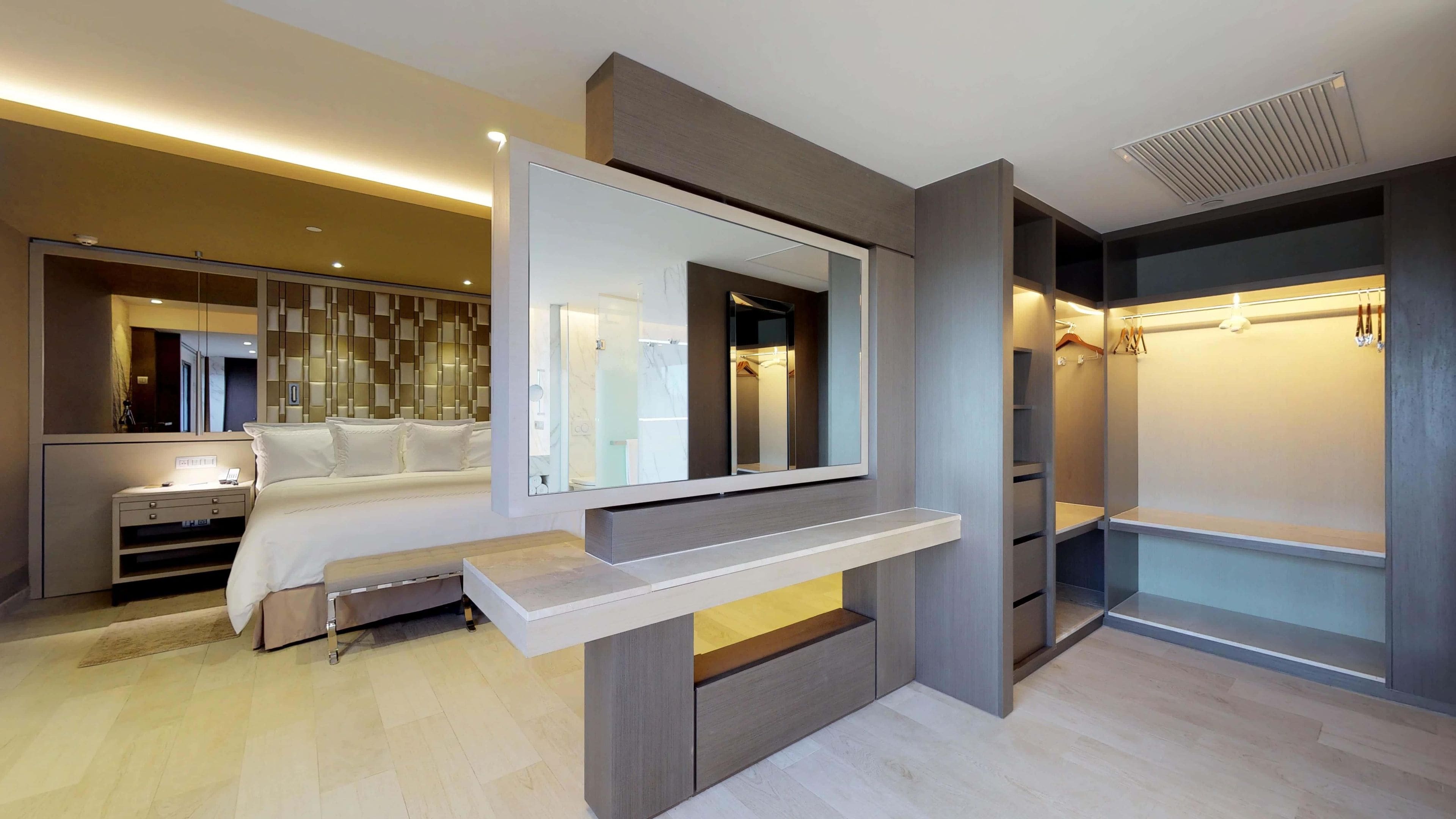 A modern hotel room with a bed, bedside table, mirror, wardrobe, and a walk-in closet.