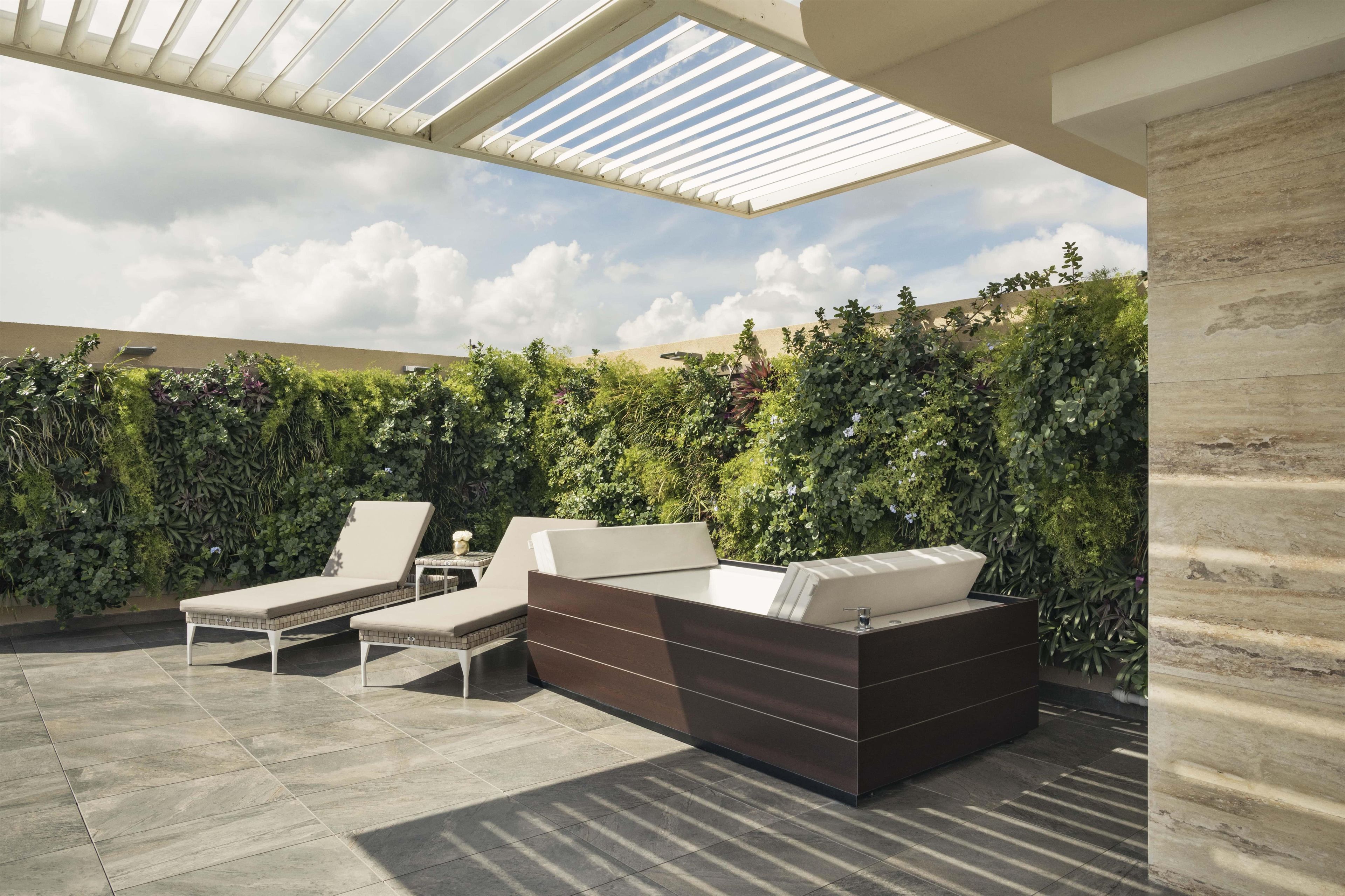 A rooftop patio with a seating area, a pergola, and a backdrop of dense foliage.