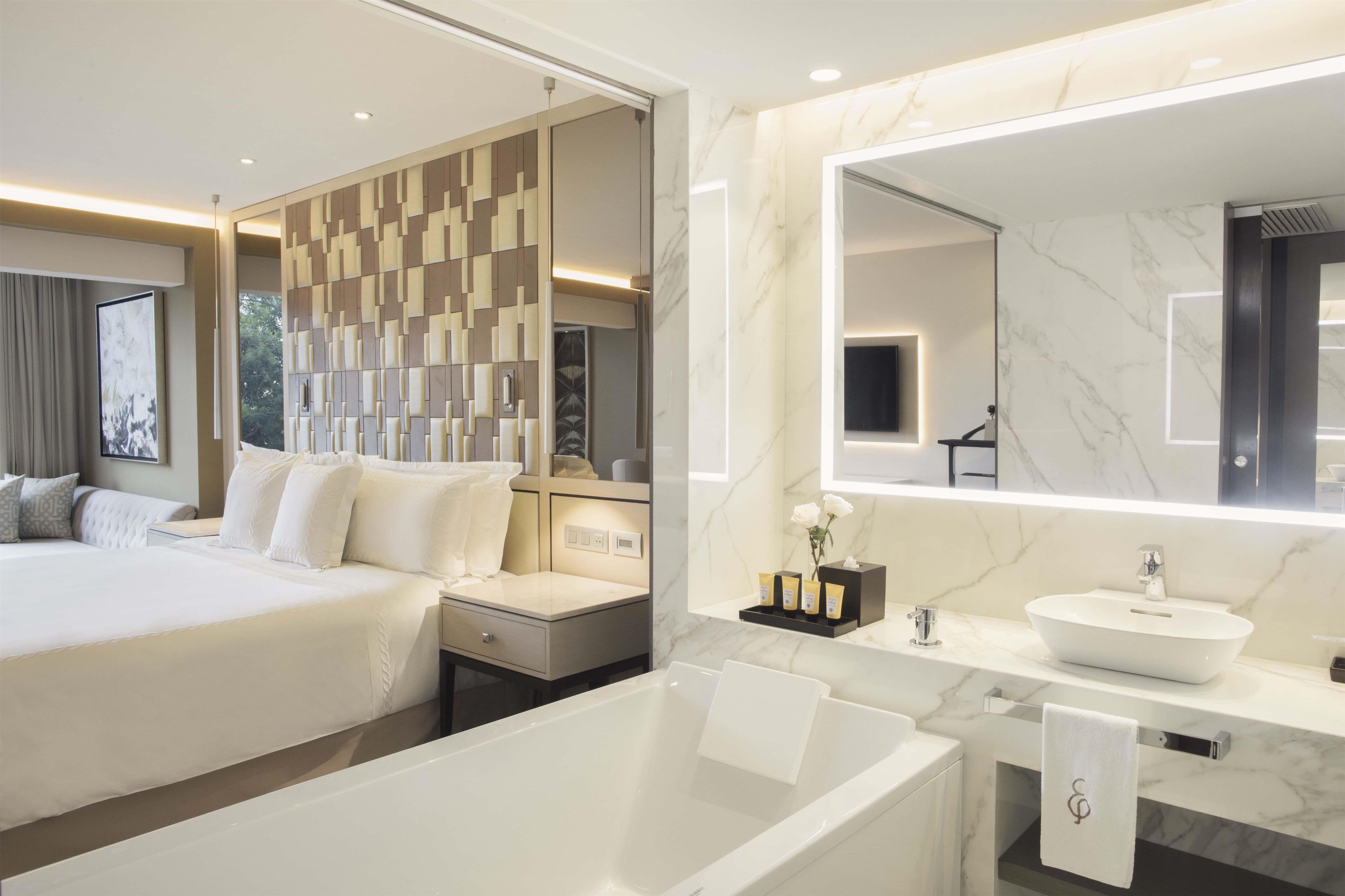 Ein modernes Hotelzimmer mit einem großen Bett, einem eigenen Badezimmer mit Badewanne und einem großen Spiegel.