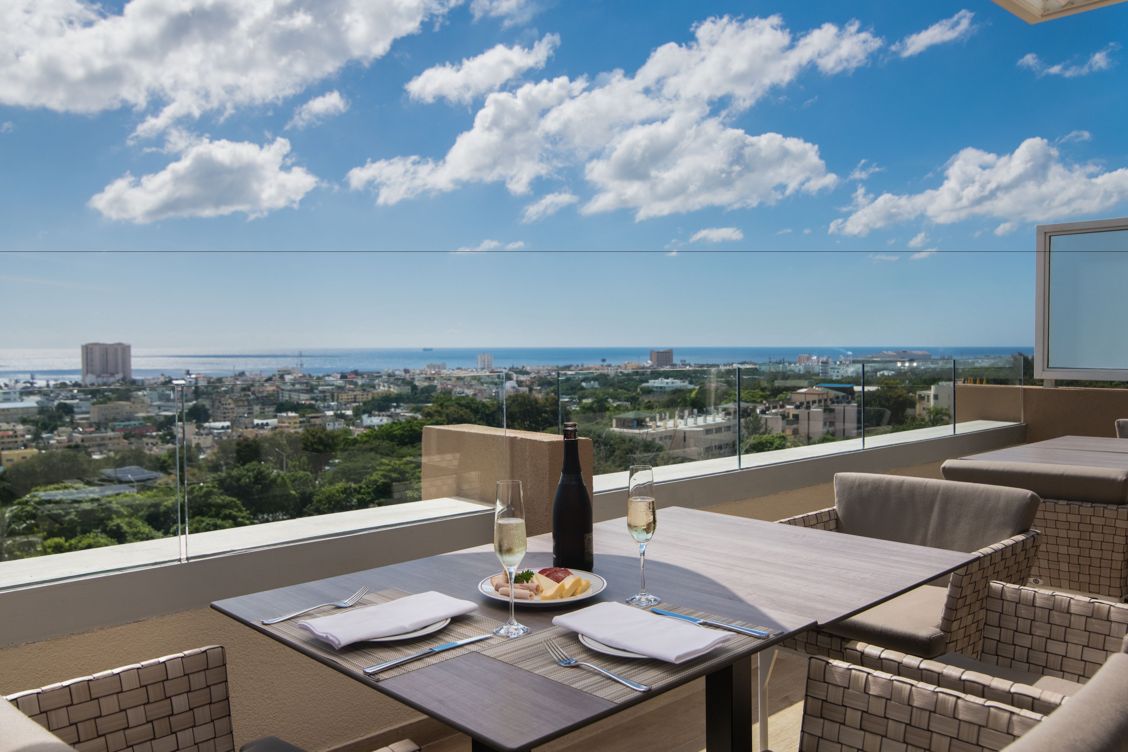 A dining area with a table set for two, overlooking a cityscape with buildings and a body of water.