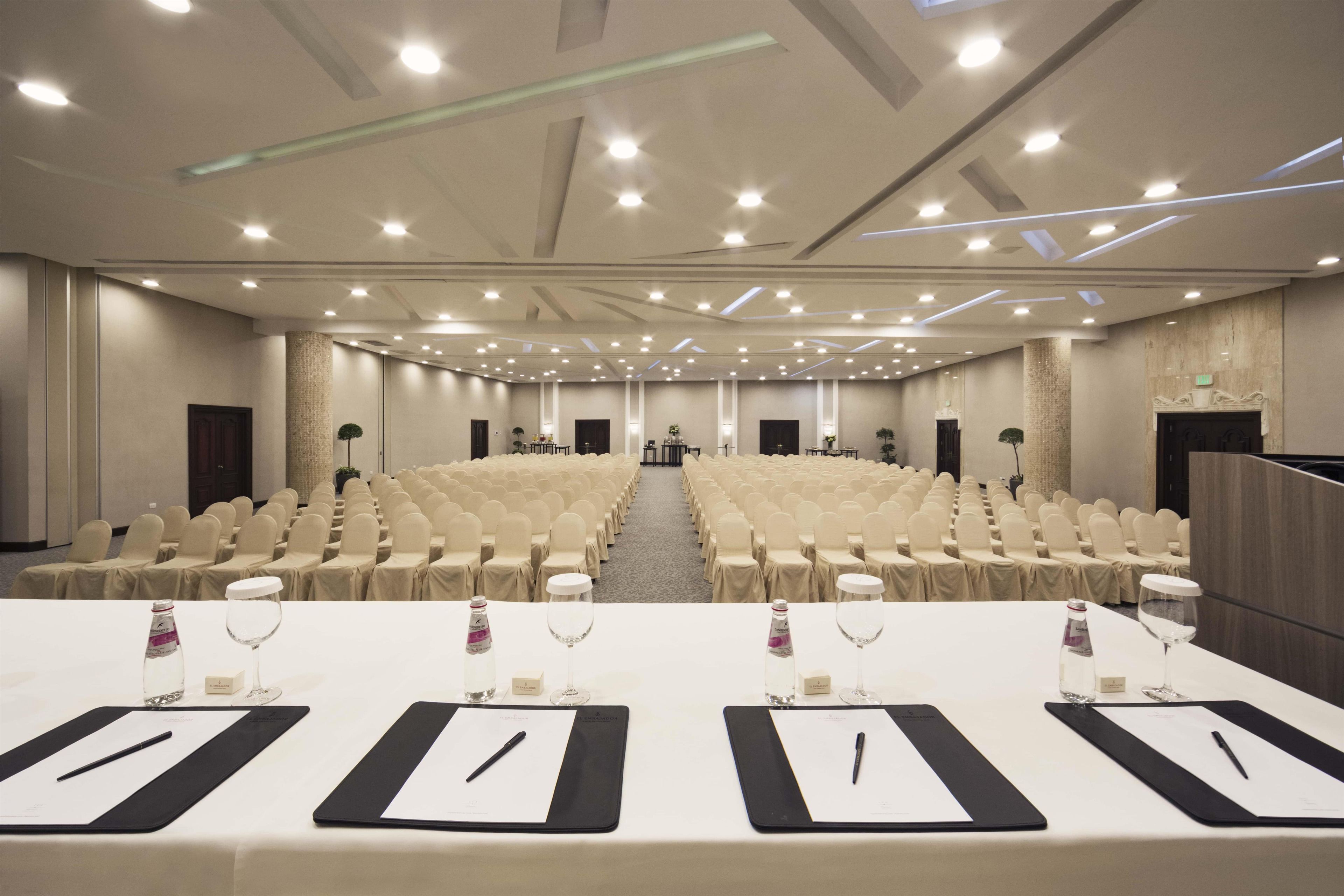 A conference room with rows of chairs, tables with nameplates, and a stage at the front.