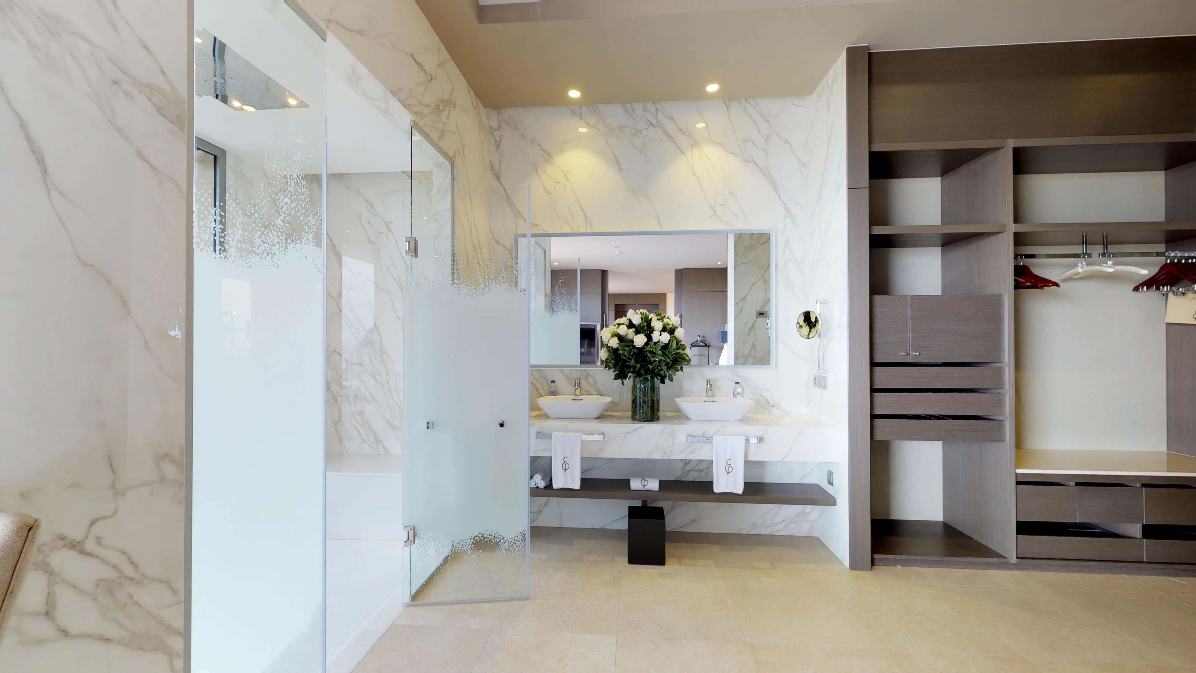 A modern bathroom with marble walls, a double sink vanity, and a walk-in closet with shelves.