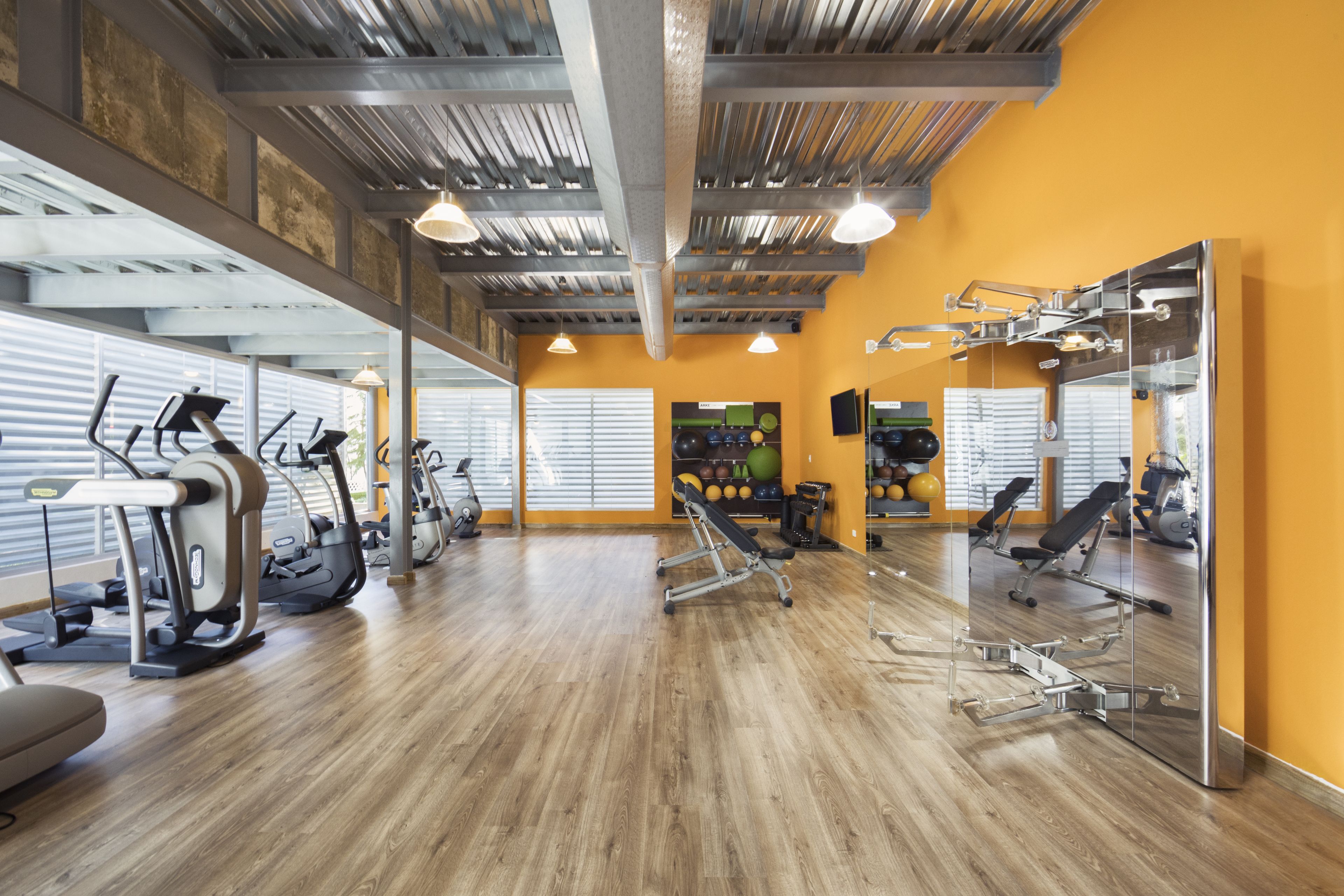 A gym with exercise equipment, a mirror, and a wooden floor.