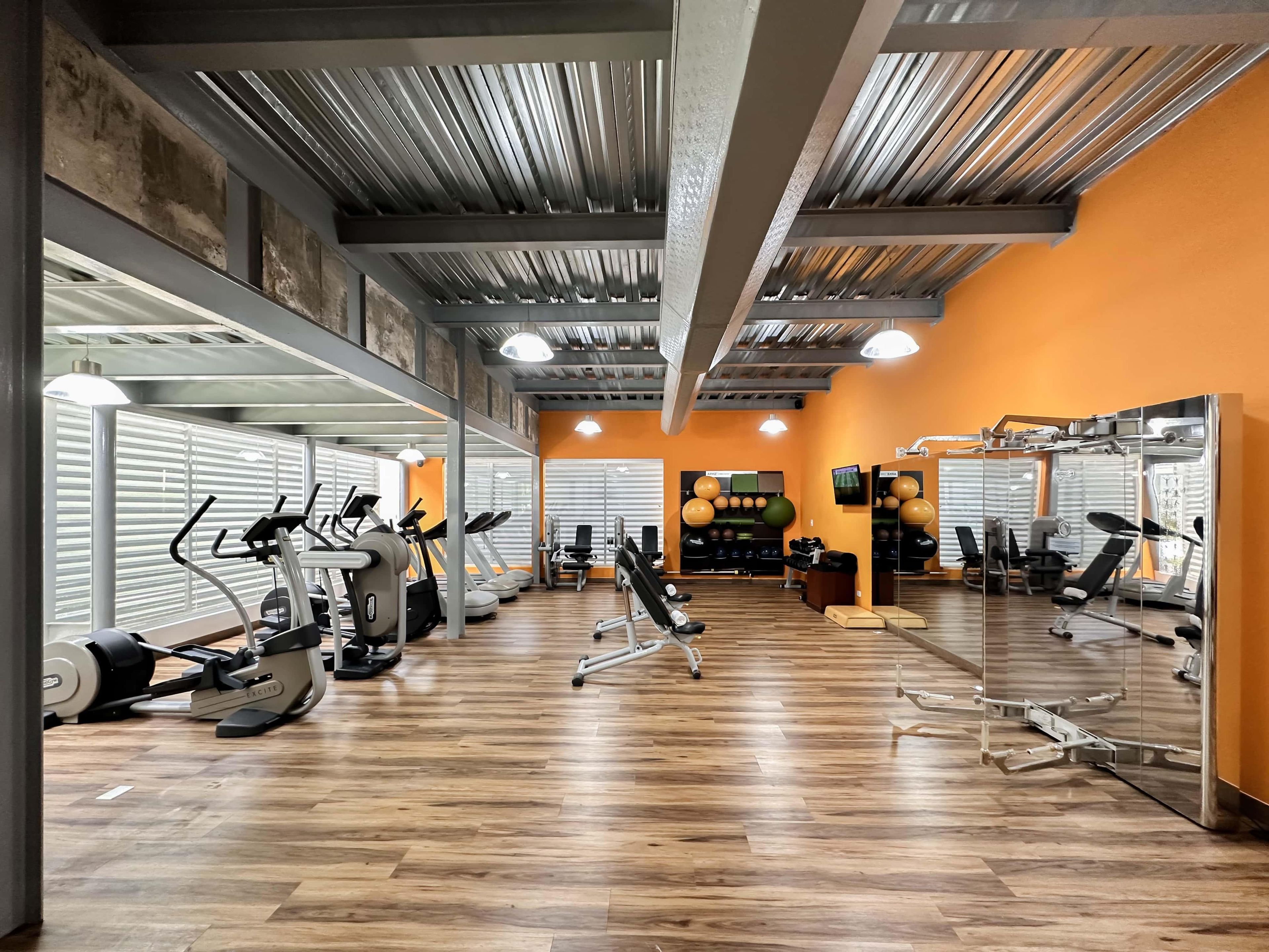 Un gimnasio con equipo de ejercicio, piso de madera y paredes anaranjadas.