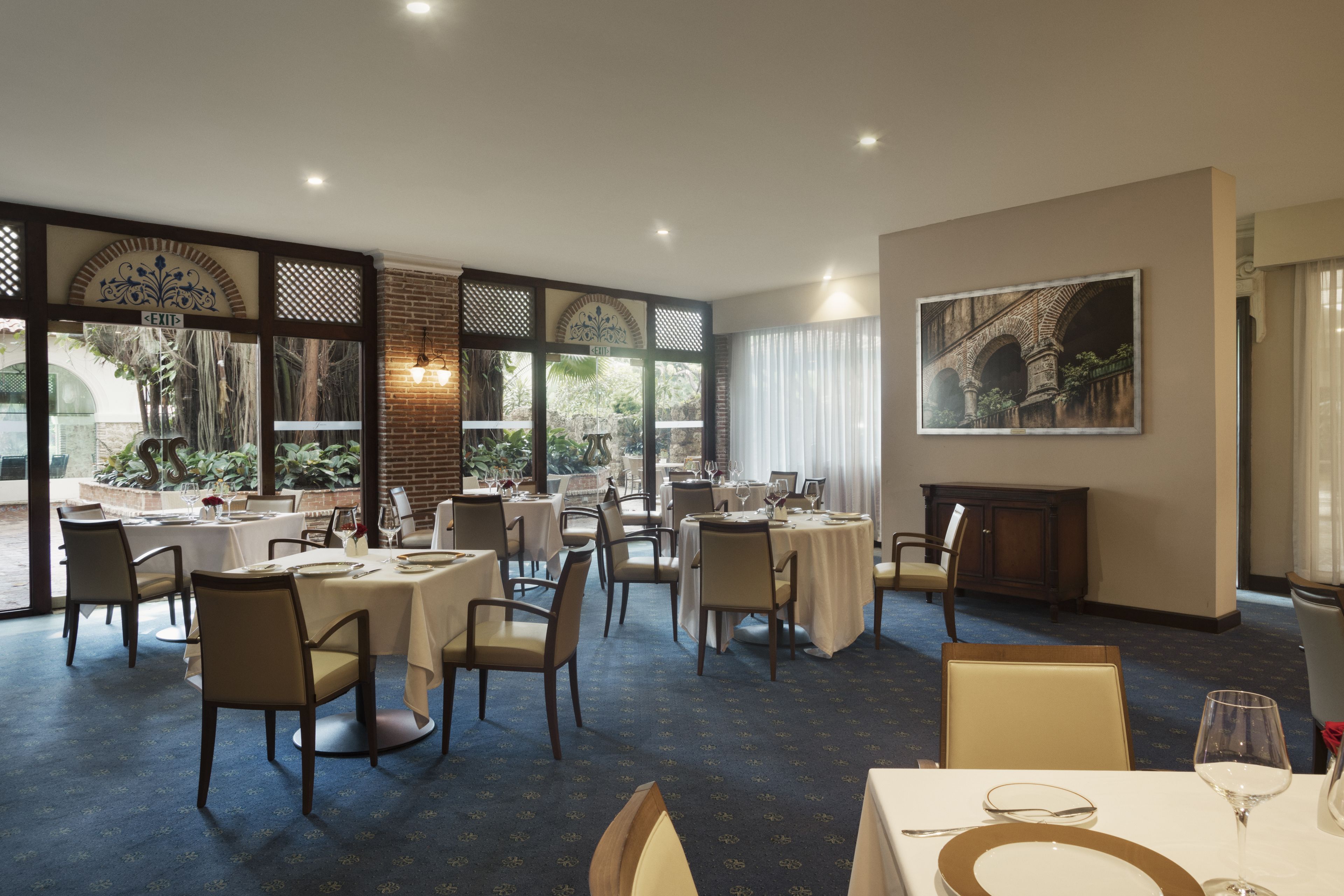 Un comedor con mesas dispuestas para el servicio, una chimenea y un ventanal con vistas a zonas verdes.