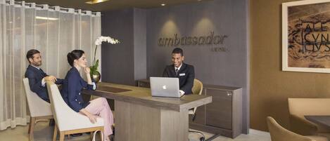 A reception desk with a nameplate reading 'Ambassador' and 'Levell'. There are three people seated on either side of the desk.